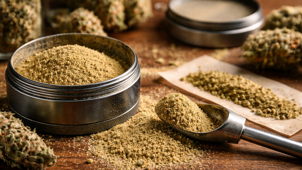 Kief powder and cannabis buds beside a metal grinder on a wooden table.