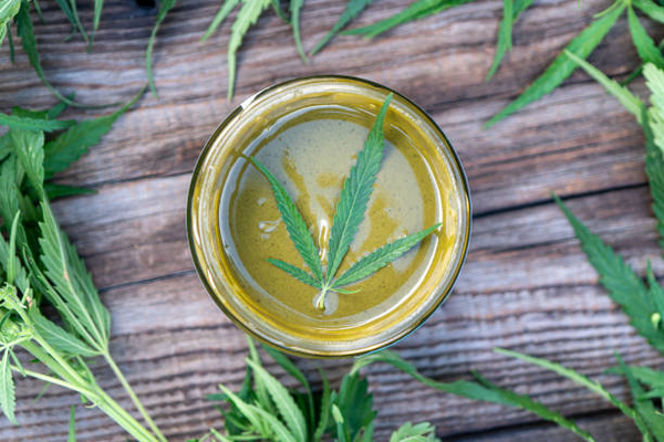 Weed butter in a glass jar with cannabis leaves on a wooden table
