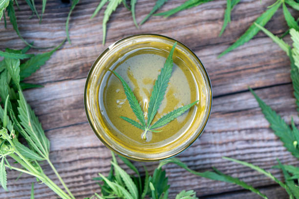 Weed butter in a glass jar with cannabis leaves on a wooden table
